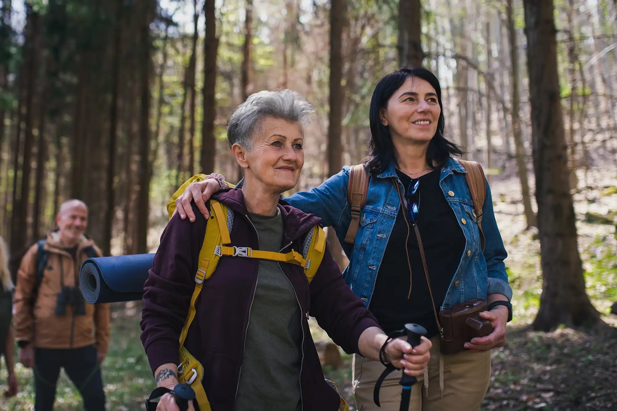 A senior mother and her middle-aged daughter hiking through a forest with a small group of friends.