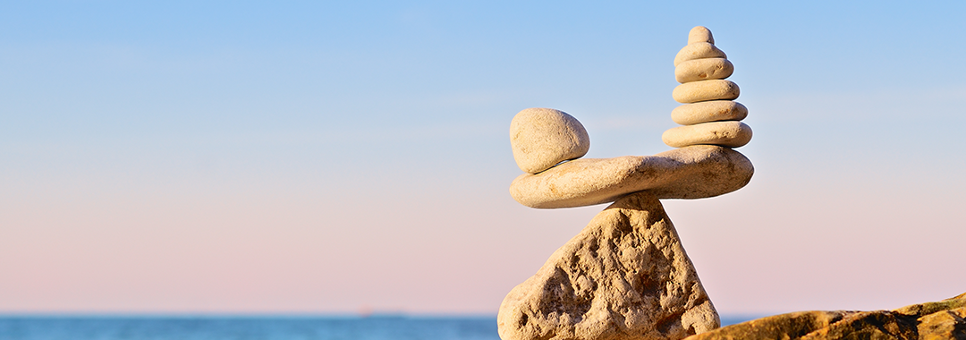 Small, stacked rocks balancing perfectly on the top of a larger rock overlooking an ocean
